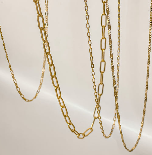 Layered gold filled paperclip chain necklace styled with delicate gold chains on a neutral background.
