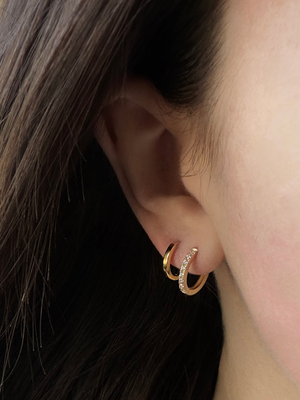 18K gold vermeil Tink huggie hoop set with cubic zirconia on a model's ear, stacked with a plain gold huggie.