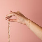 Gold filled paperclip chain bracelet on a model's wrist, holding a chain, soft pink background.