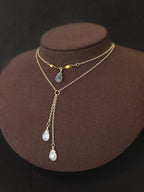 Gold filled lariat with a grey stone drop and two teardrop drops on a display bust.