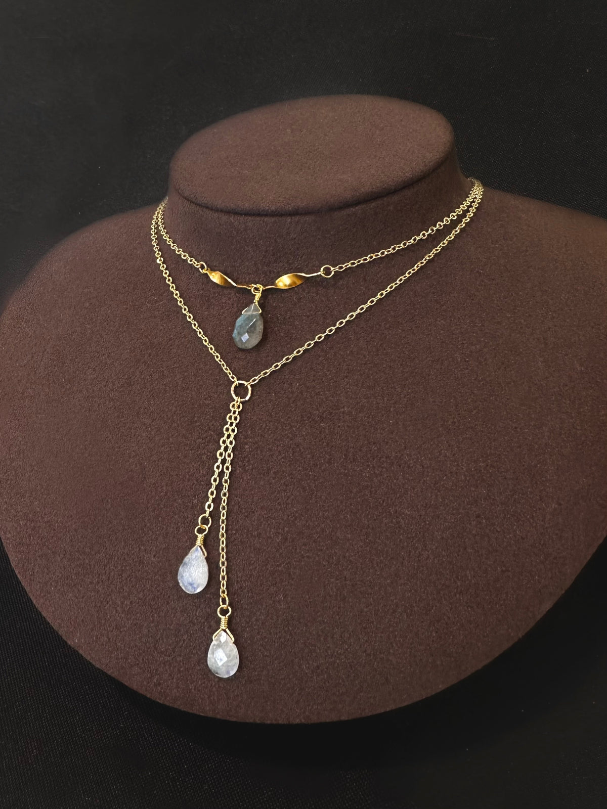 Gold filled lariat with a grey stone drop and two teardrop drops on a display bust.