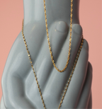 Gold filled Wave chain with twisted detailing draped over a ceramic hand, pink background.