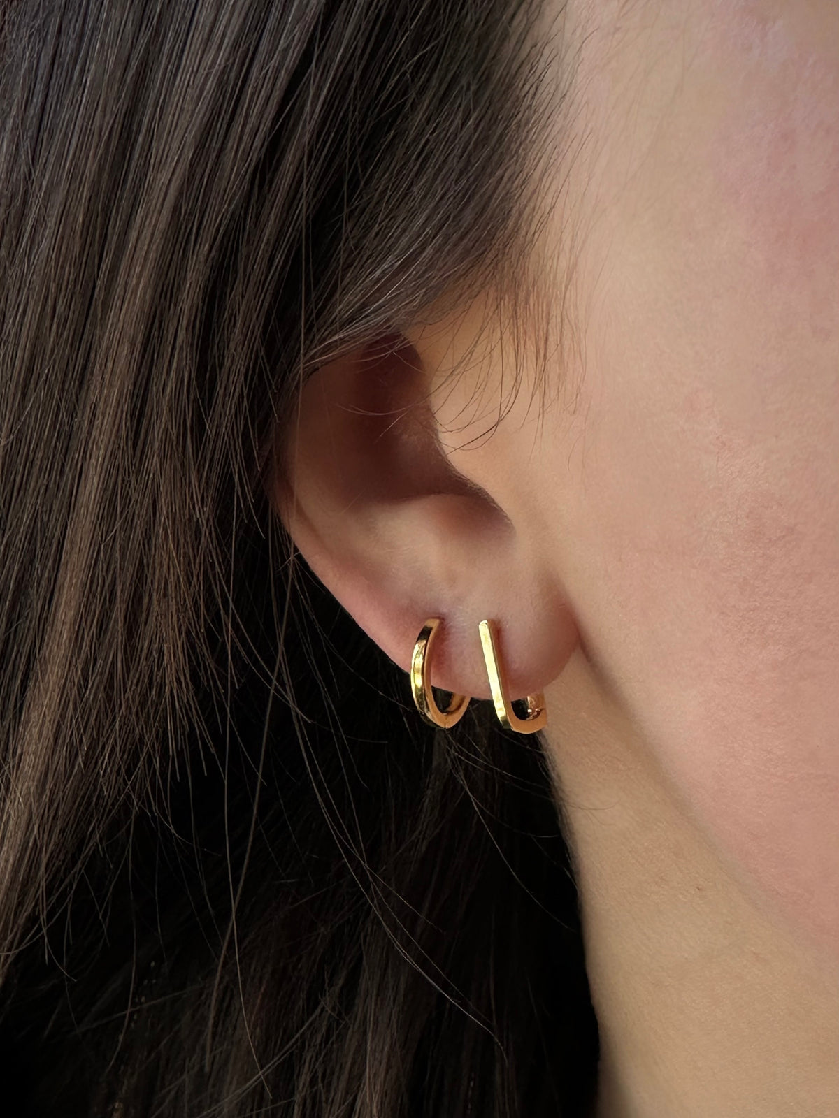 18K gold vermeil tiny oval huggie hoops stacked on a model's ear.