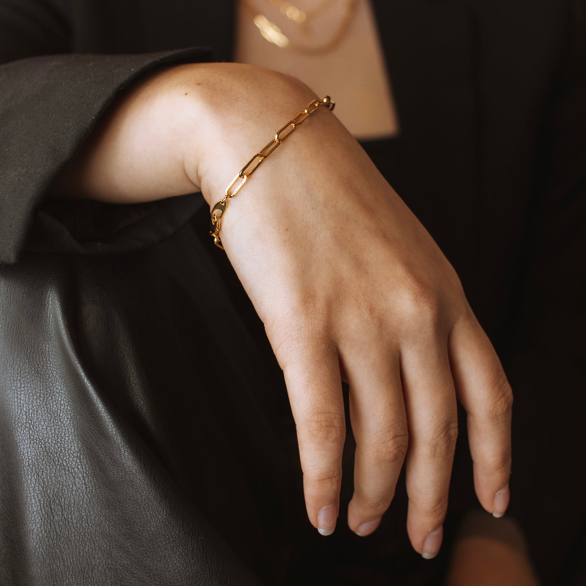 Florence gold filled paperclip chain bracelet on a model's wrist resting on black leather.