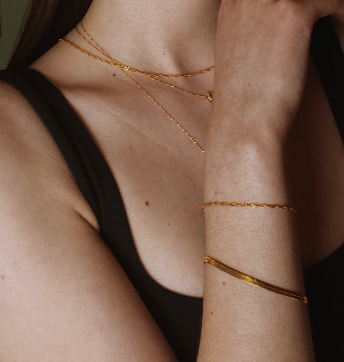 Gold herringbone bracelet layered with a rope-chain bracelet and gold necklaces on a model.