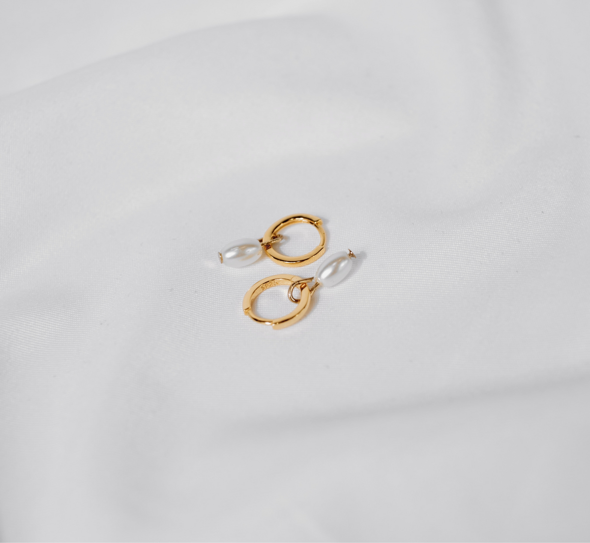 Pair of Tiny Pearl huggie hoops in 18K gold vermeil, each with a freshwater pearl drop, on white silk.