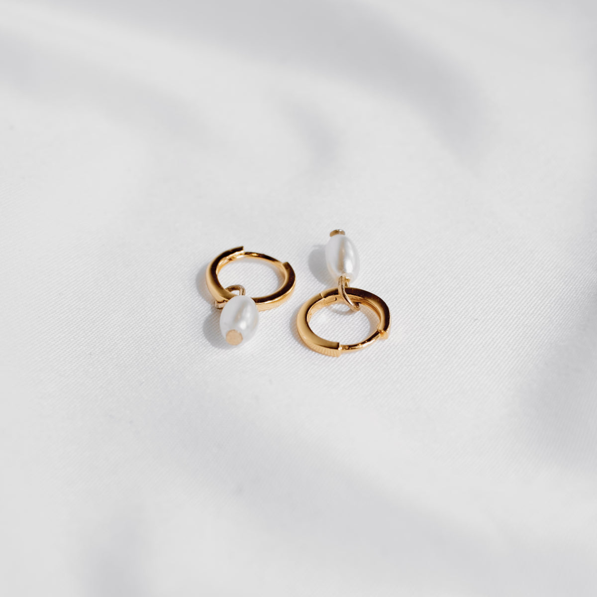 Gold vermeil Tiny Pearl huggie hoops with freshwater pearl drops on white silk.