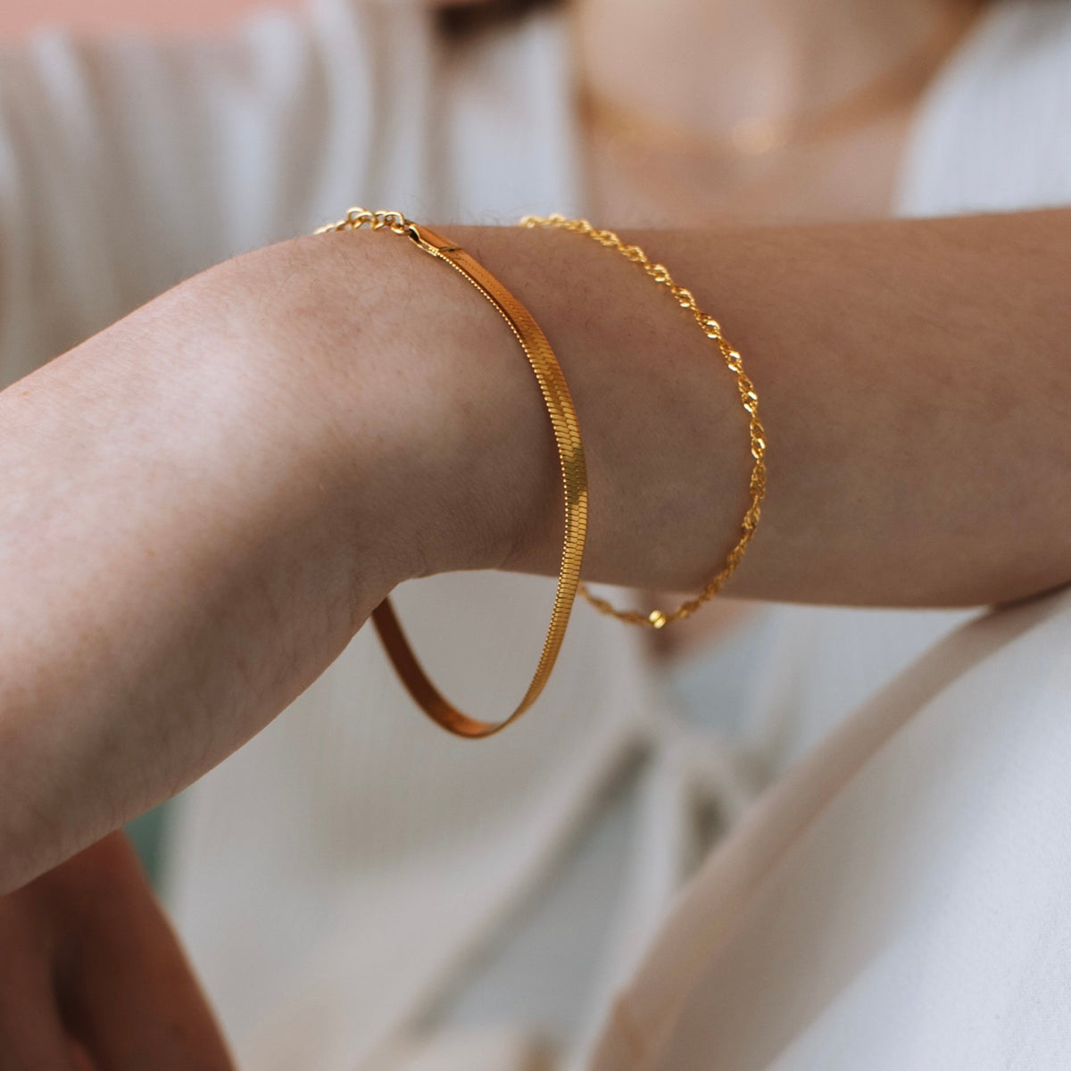 Gold plated stainless steel herringbone bracelet stacked with a rope-chain bracelet on a model's wrist.
