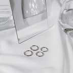 Four silver-tone stainless steel classic hoops clustered on white fabric beside a mirror.