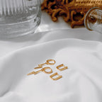 Gold vermeil oval huggie hoops with lightning-bolt charm earrings on white beside an ornate gold frame.