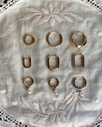 Flat-lay of gold and silver huggie hoops in several styles on embroidered linen.