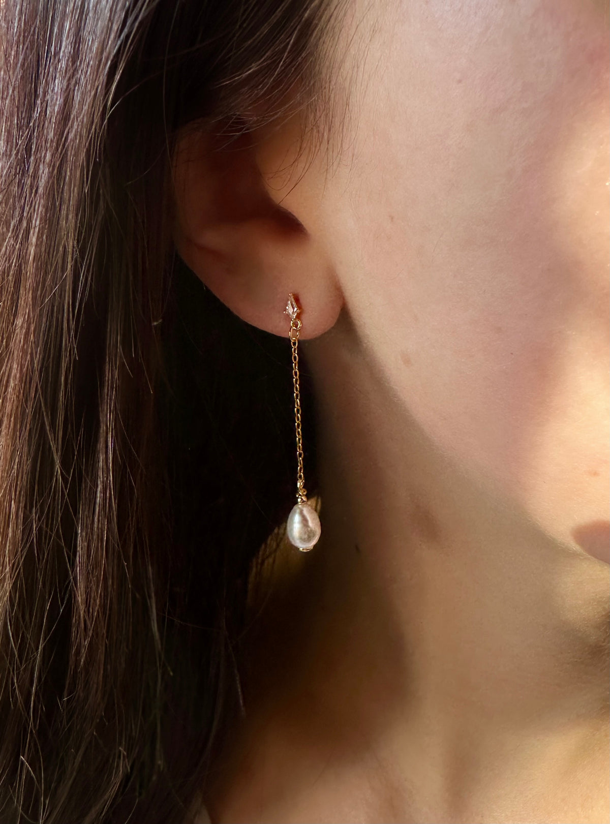 Dove drop earring in 18K gold vermeil on a model's ear, a marquise-cut zirconia on a fine chain ending in a freshwater pearl.
