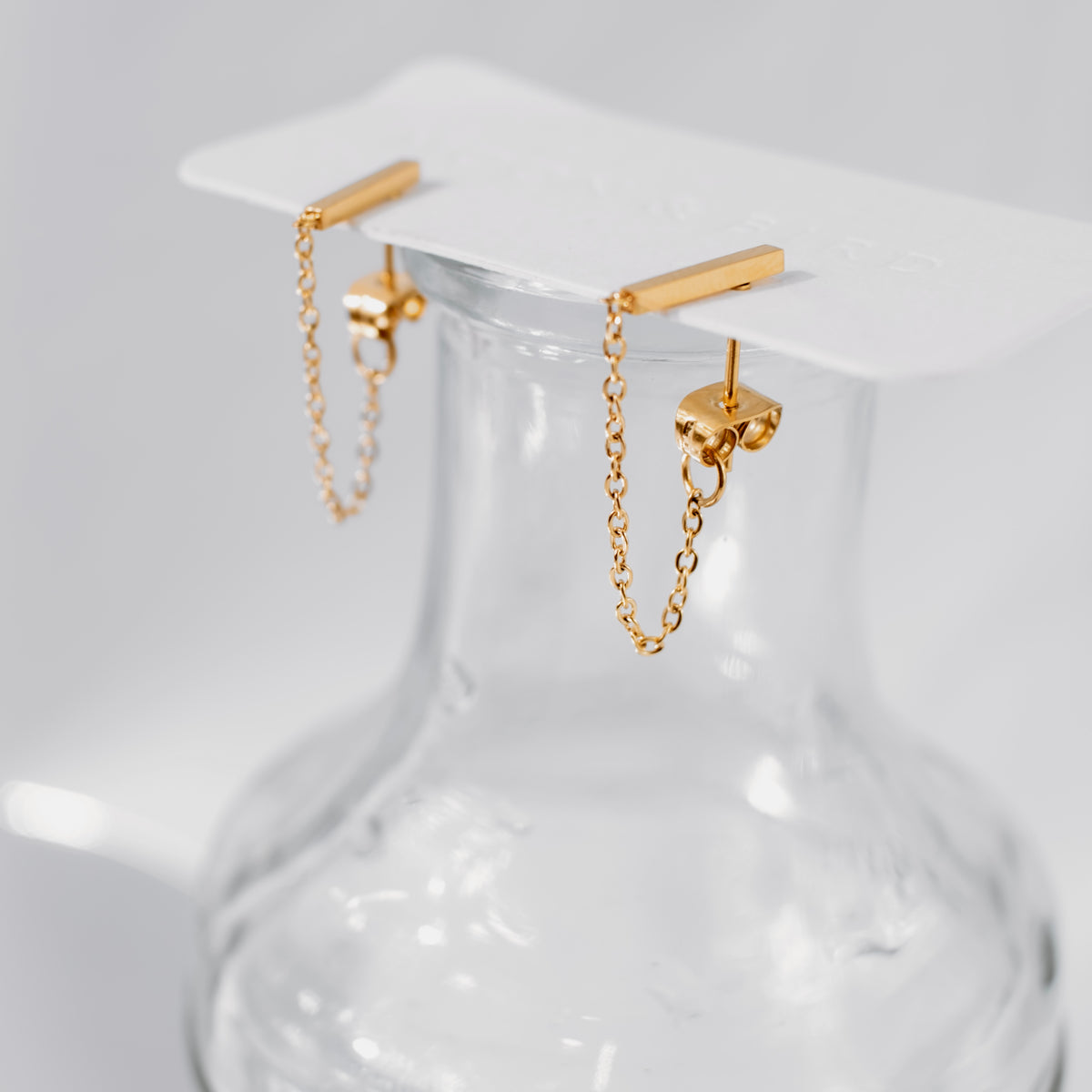 Pair of 18K gold vermeil bar chain-link stud earrings hooked over the rim of a clear glass vase.