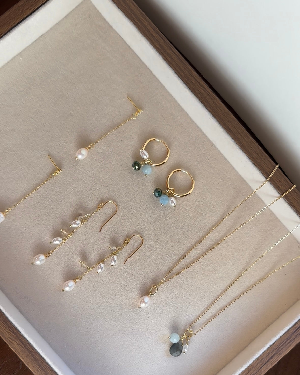Flat-lay of 18K gold vermeil drop earrings and a necklace with freshwater pearls and pale gemstones on an ivory tray.