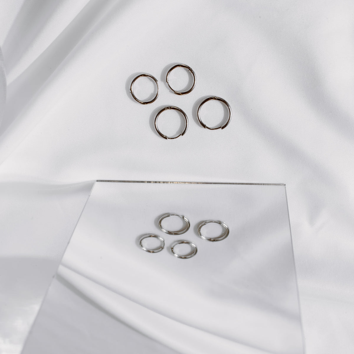 Silver-tone stainless steel classic hoops on white fabric with a mirror reflection.