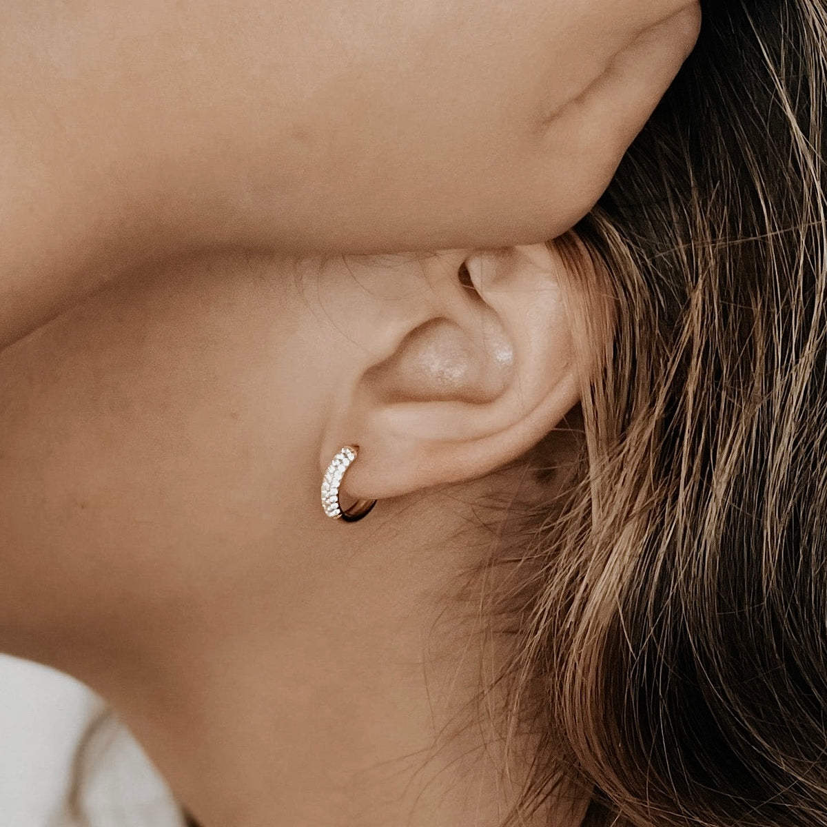 Sage pave cubic zirconia huggie hoop on a model's ear.