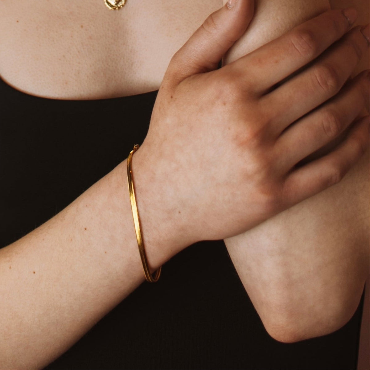 Clementine flat herringbone bracelet in gold plated stainless steel on a model's wrist.