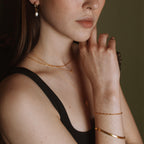 Model wearing an 18K gold vermeil pearl drop hoop with layered gold necklaces and bangles.