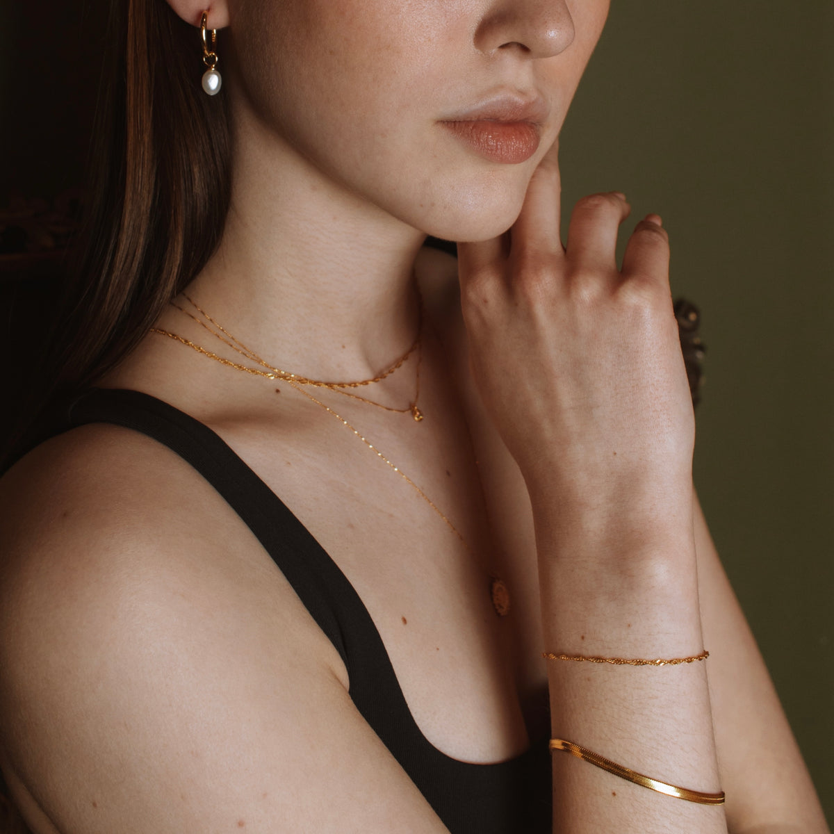 Model wearing an 18K gold vermeil pearl drop hoop with layered gold necklaces and bangles.