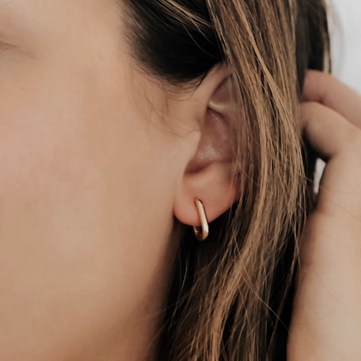 Oval hoop in gold plated stainless steel on a model's ear.