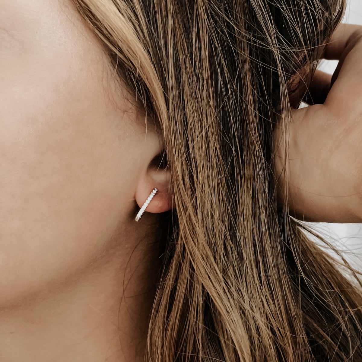 A sterling silver oval huggie hoop on a model's ear.