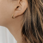 Gold plated stainless steel oval hoop on a model's ear.
