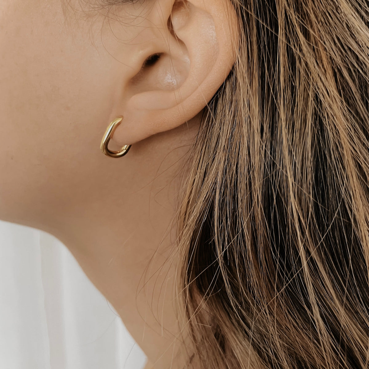 Gold plated stainless steel oval hoop on a model's ear.