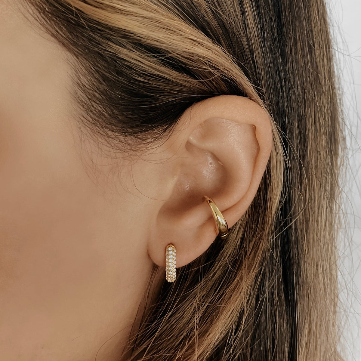 18K gold vermeil Sage huggie hoop set with cubic zirconia on a model's ear, worn with a gold ear cuff.