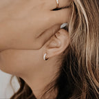 18K gold vermeil Sage pave cubic zirconia huggie hoop on a model's ear.