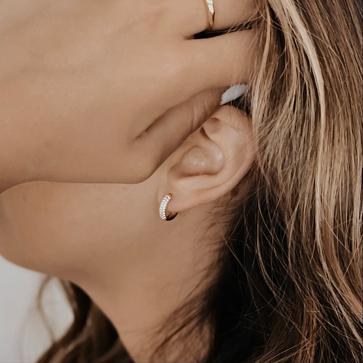 18K gold vermeil Sage pave cubic zirconia huggie hoop on a model's ear.