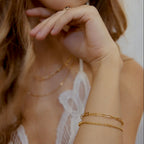 Gold filled paperclip chain bracelet on a model's wrist with a white lace top.