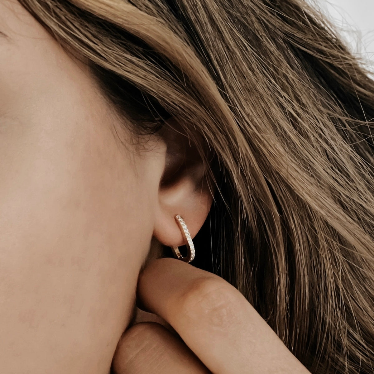 An 18K gold vermeil oval huggie hoop on a model's ear.