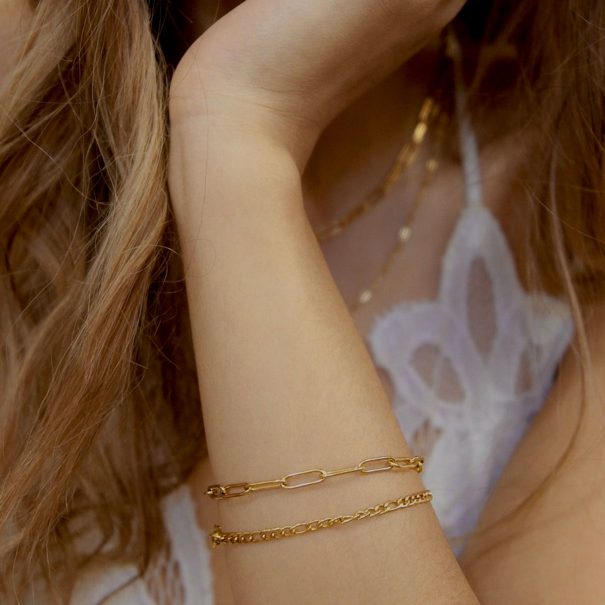 Gold filled paperclip chain bracelet layered with a finer chain on a model's wrist.