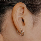 Sterling silver Wave huggie hoops with a twisted design stacked on a model's ear.