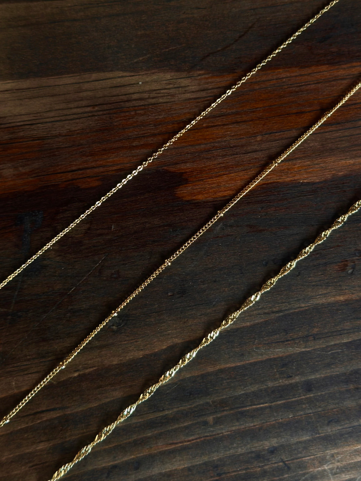 Gold filled Wave chain with twisted, wave-like detailing on a wooden surface.