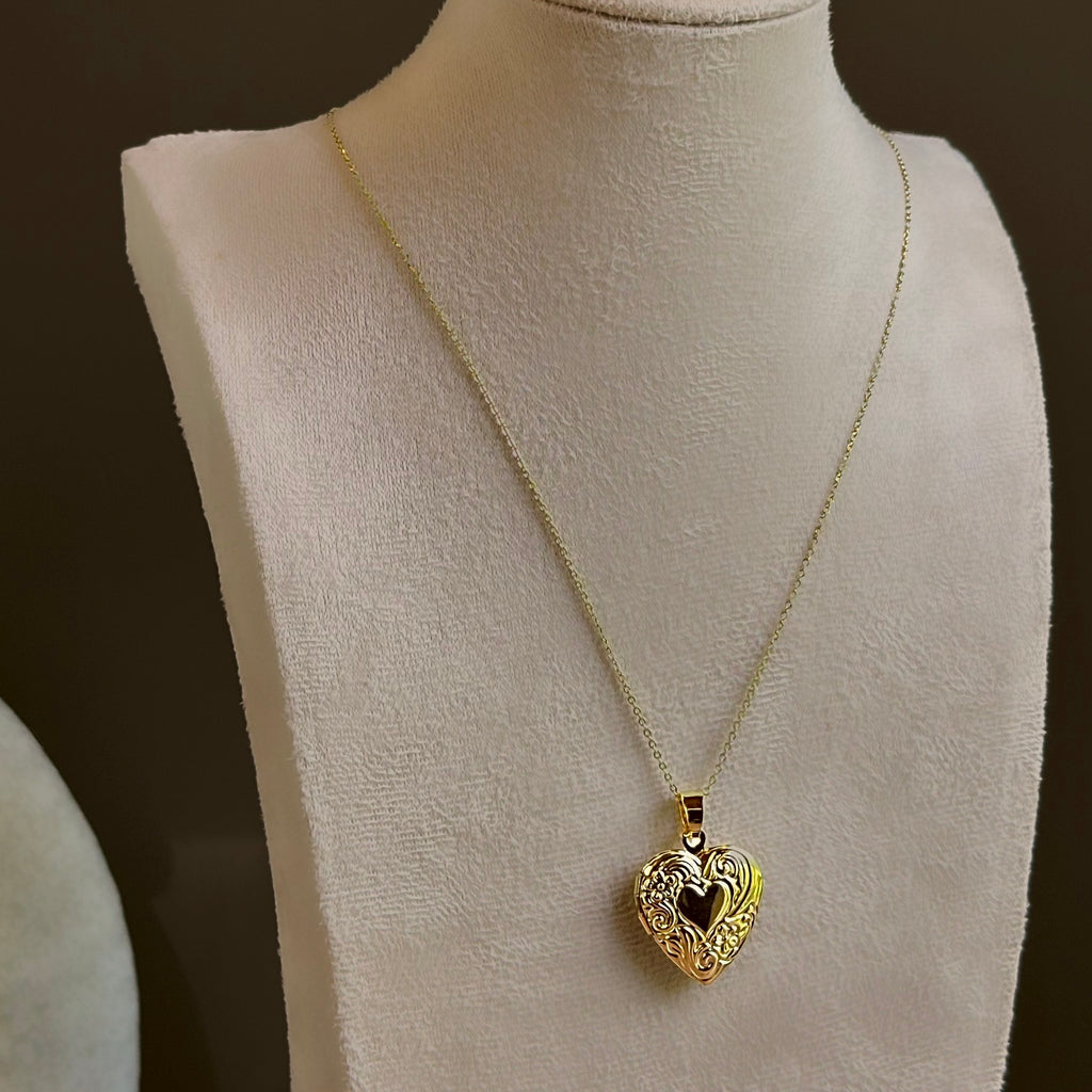 Large Heart locket with scrollwork around a dark heart centre, on a fine satellite chain on an ivory bust.
