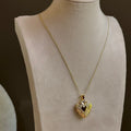 Large Heart locket with scrollwork around a dark heart centre, on a fine satellite chain on an ivory bust.