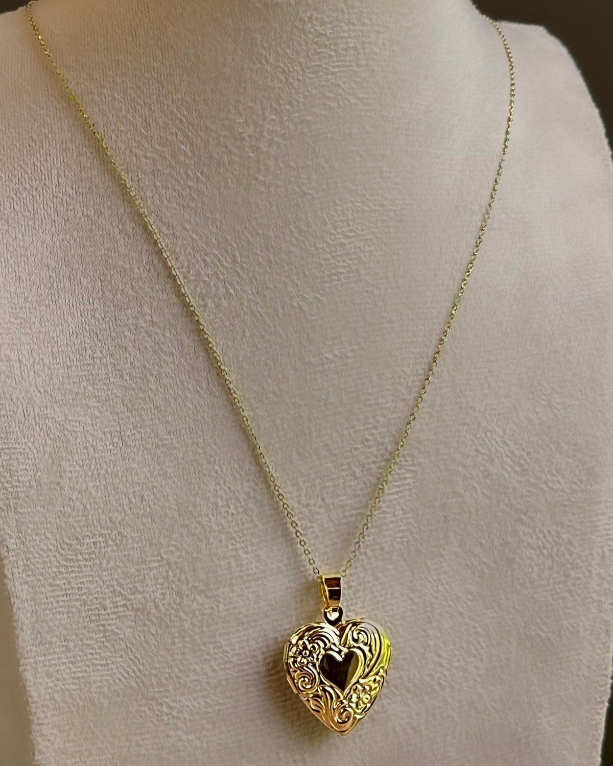 Large Heart locket with scrollwork around a dark heart centre, on a fine satellite chain on an ivory bust.