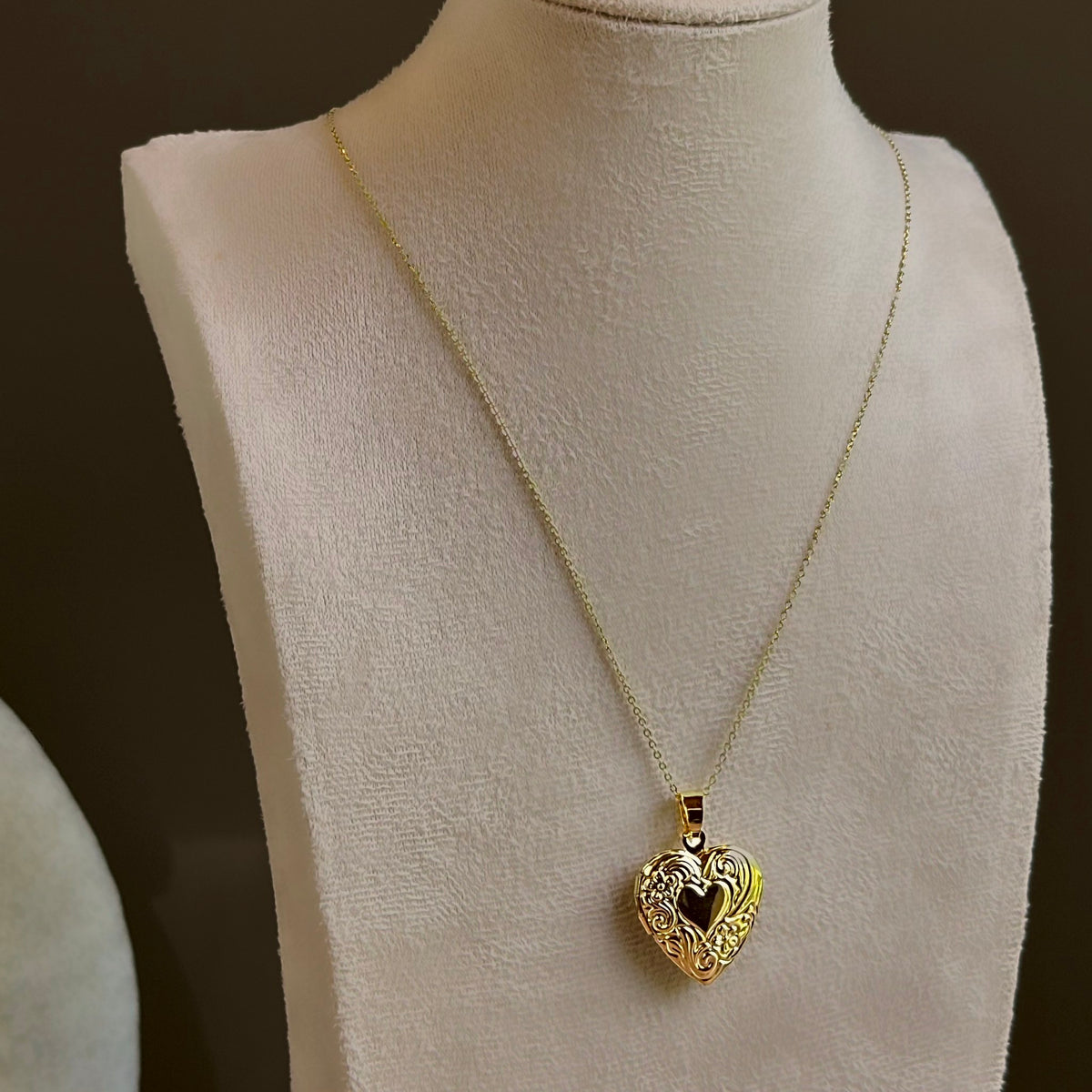 Large Heart locket with scrollwork around a dark heart centre, on a fine satellite chain on an ivory bust.