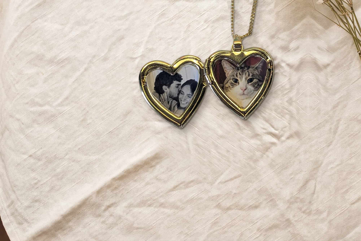 An open heart locket on ivory linen, one side printed with a couple, the other with a cat.