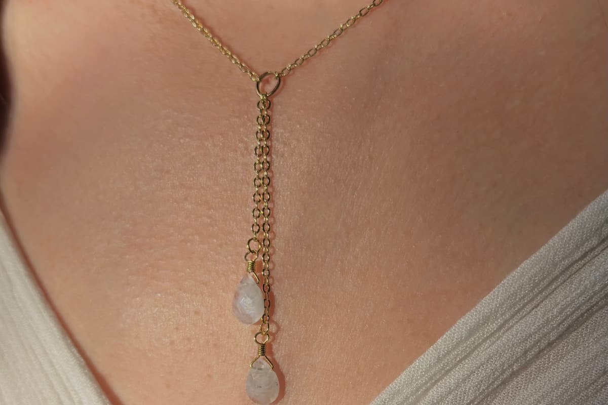A lariat necklace with two pale teardrop stones, worn at the collarbone.