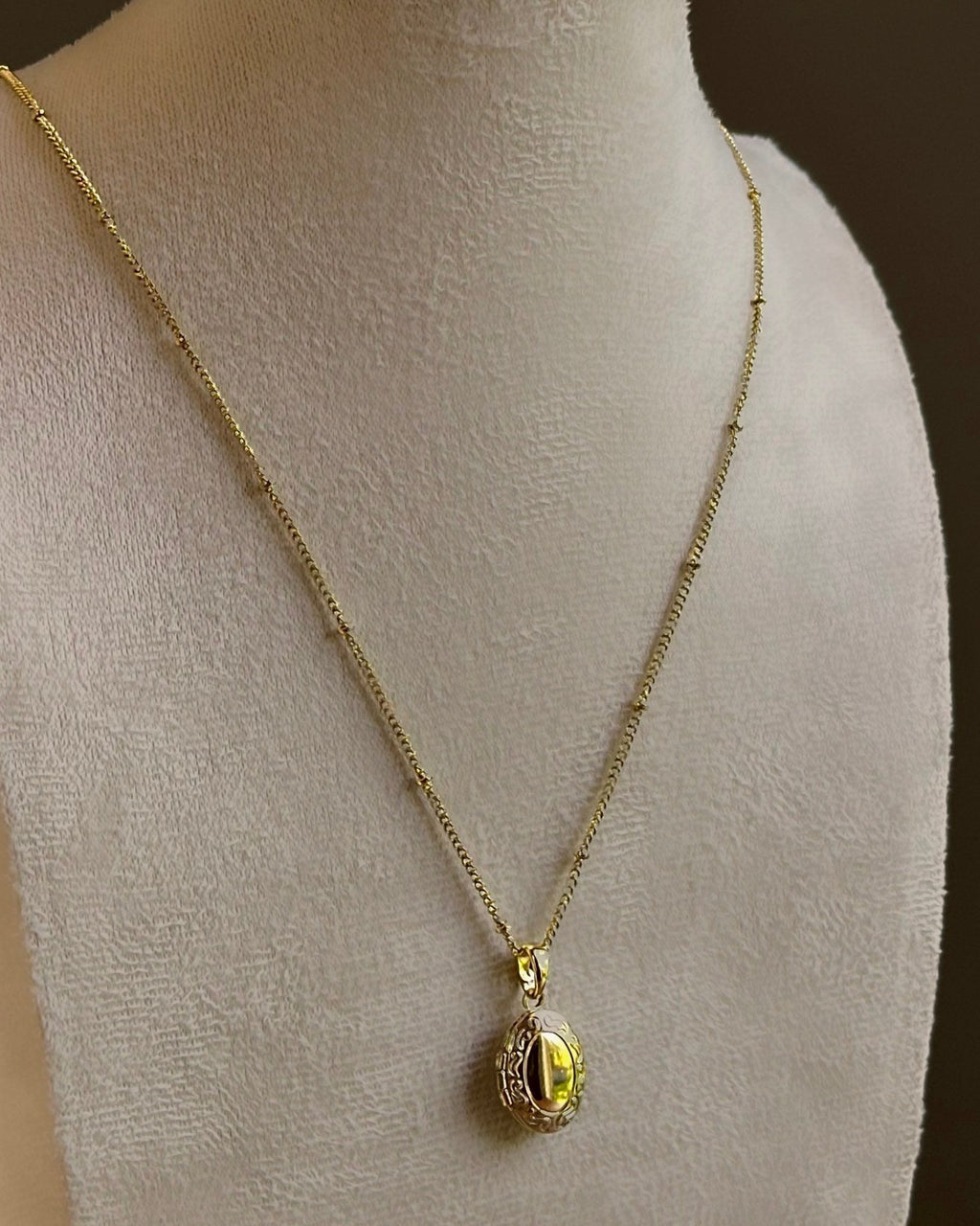 Oval locket with an engraved frame, on a fine satellite chain on an ivory bust.