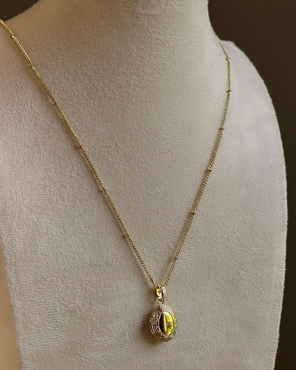 Oval locket with an engraved frame, on a fine satellite chain on an ivory bust.
