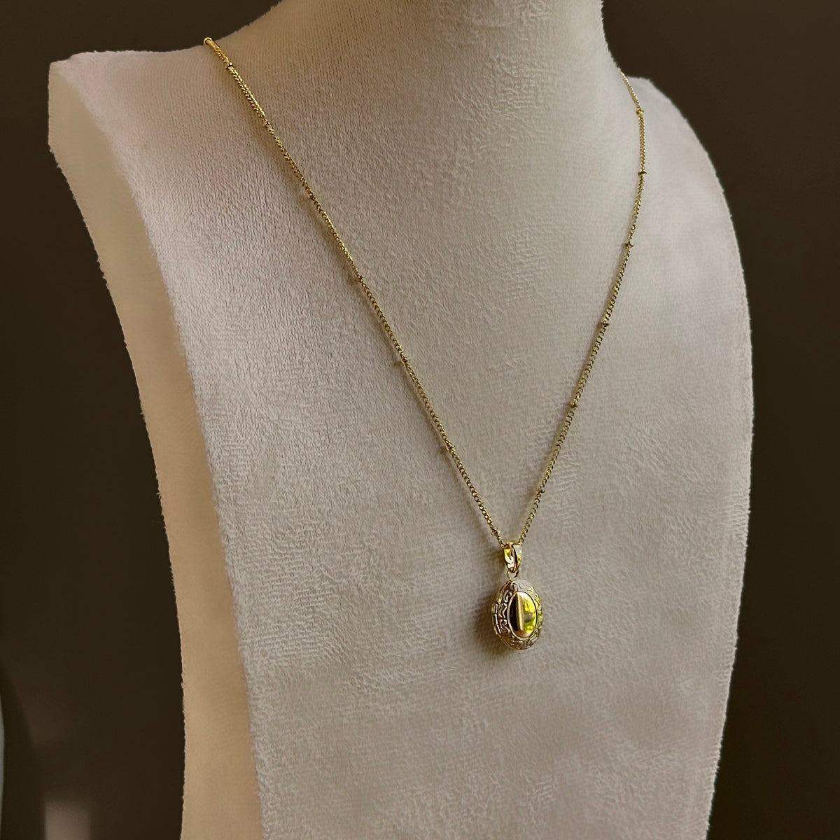 Oval locket with an engraved frame, on a fine satellite chain on an ivory bust.