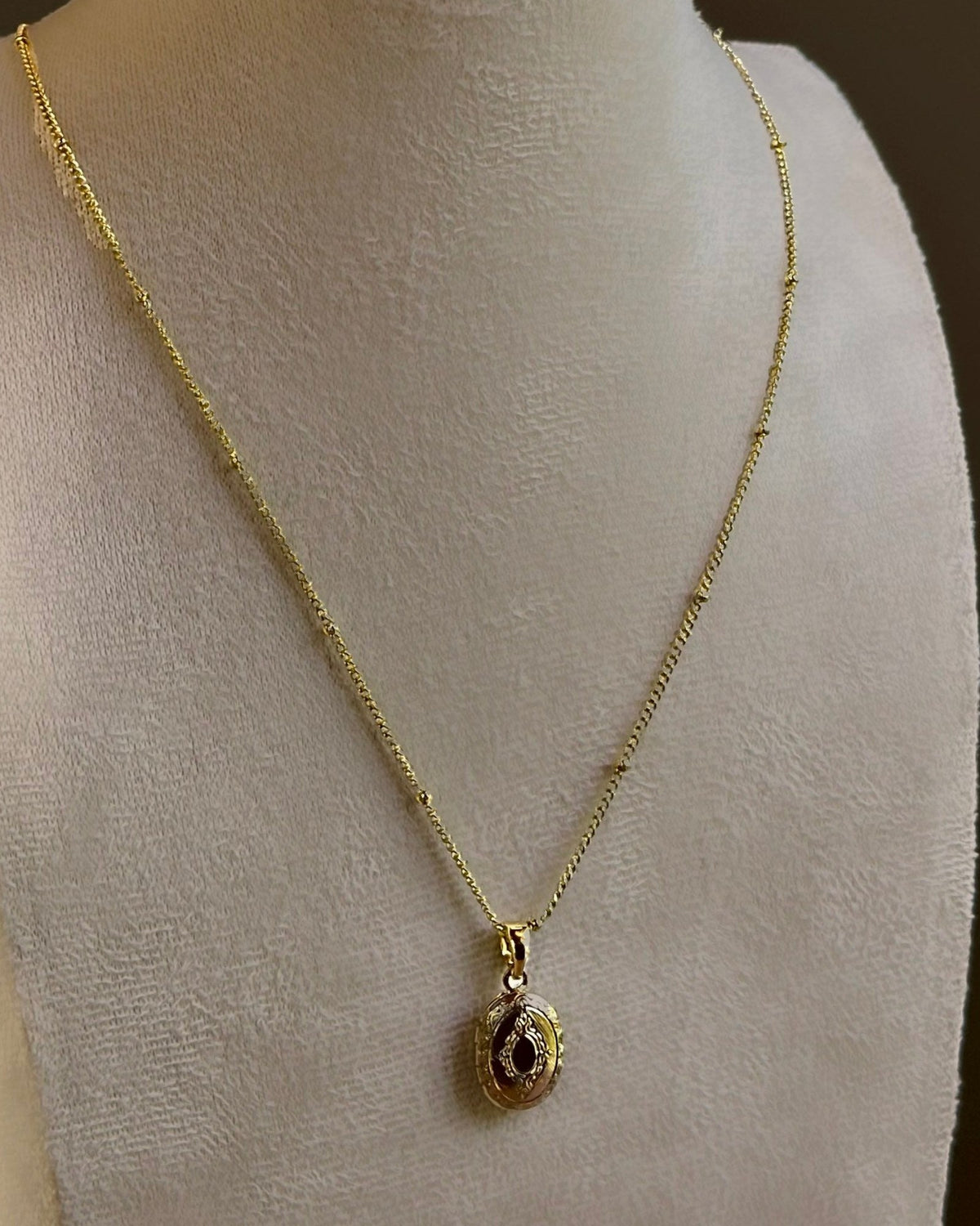 Small Ornate Oval locket on a fine satellite chain, on an ivory bust.
