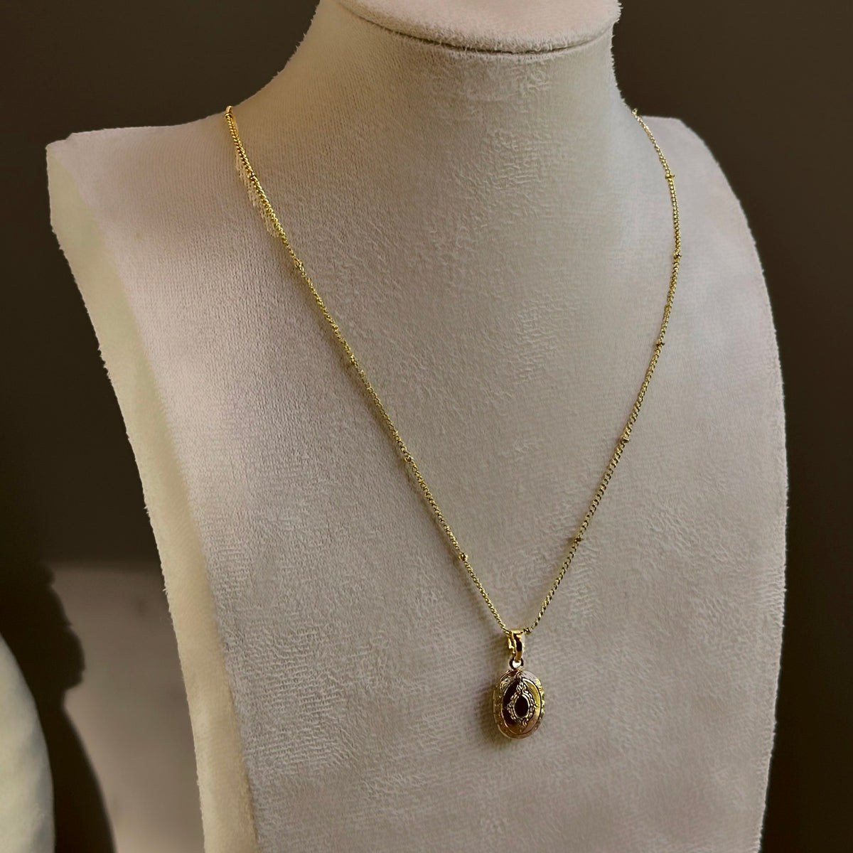Small Ornate Oval locket on a fine satellite chain, on an ivory bust.