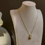 Small Ornate Oval locket with its pearl charm, on a satellite chain on an ivory bust.